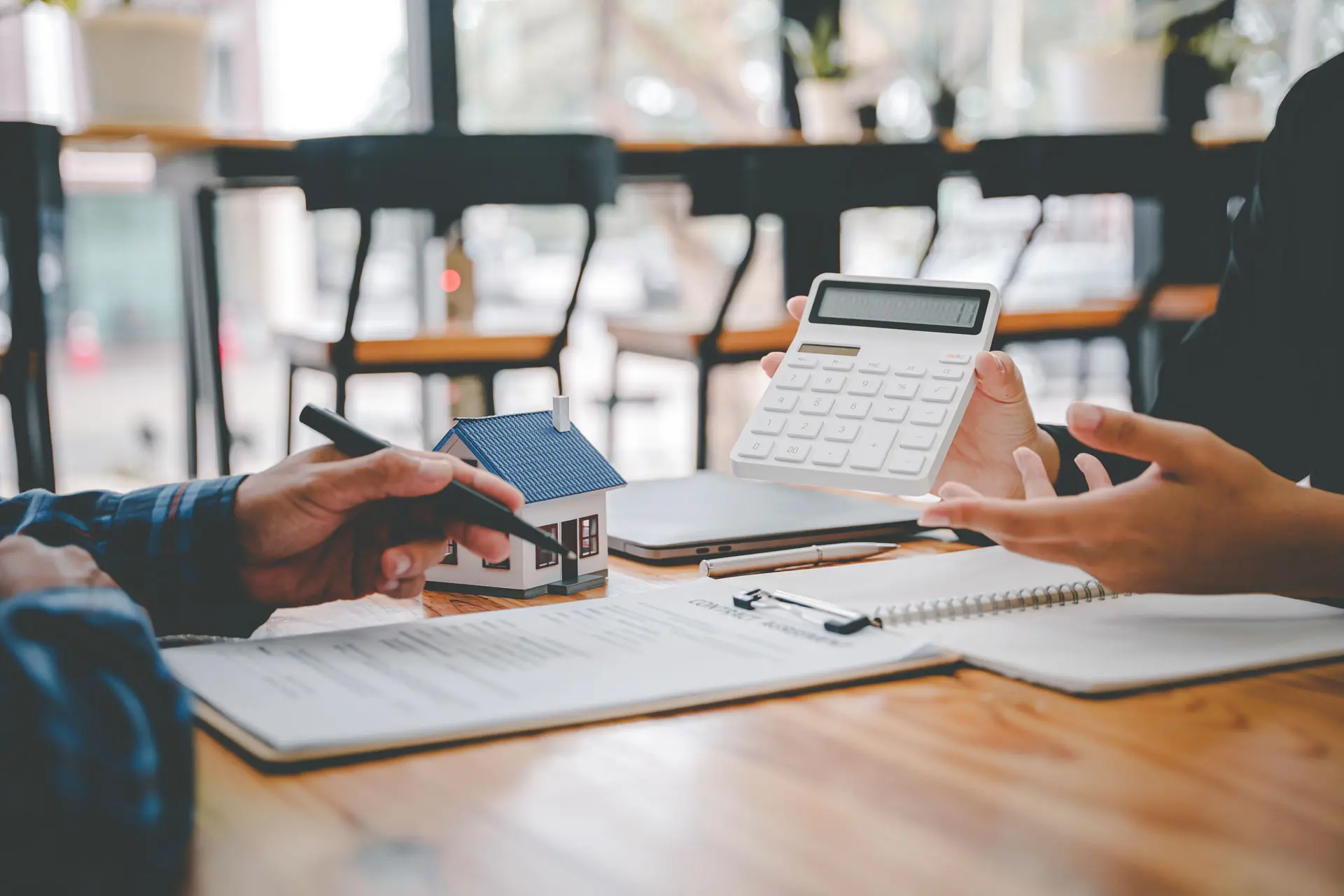 Zwei Personen sitzen am Tisch mit Unterlagen. Die eine Person zeigt auf einem Taschenrechner einen Zahl für die Bewertung eines Objekts.
