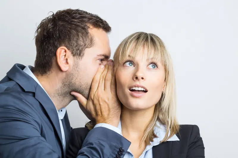 Zwei Personen stehen nebeneinander, eine Person flüstert der anderen etwas ins Ohr – symbolisiert das Weitergeben eines Tipps oder einer Empfehlung im Immobilienbereich.